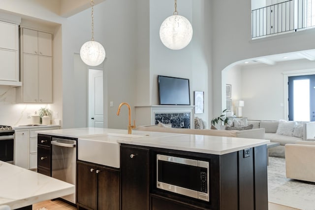 kitchen featuring a towering ceiling, stainless steel appliances, decorative light fixtures, and white cabinets