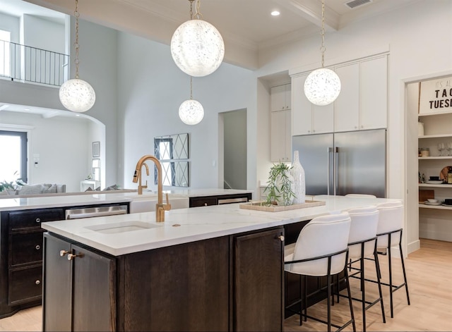 kitchen featuring sink, built in refrigerator, a kitchen island with sink, hanging light fixtures, and white cabinets