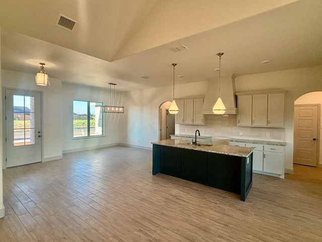 kitchen featuring pendant lighting, white cabinetry, sink, custom range hood, and a center island with sink