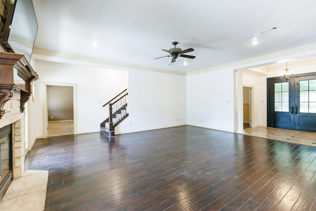 unfurnished living room featuring crown molding, a premium fireplace, dark hardwood / wood-style floors, ceiling fan with notable chandelier, and french doors