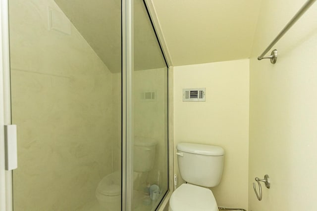 bathroom featuring a shower with door and toilet