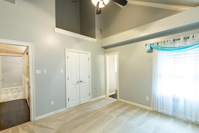 unfurnished bedroom with ceiling fan, a towering ceiling, light colored carpet, and a closet