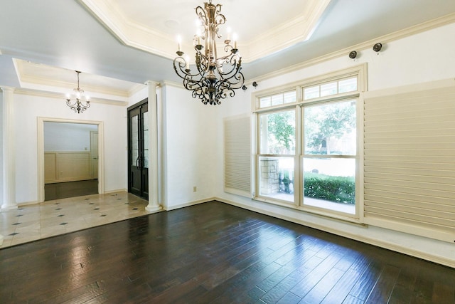 unfurnished room with a tray ceiling, plenty of natural light, decorative columns, and a chandelier