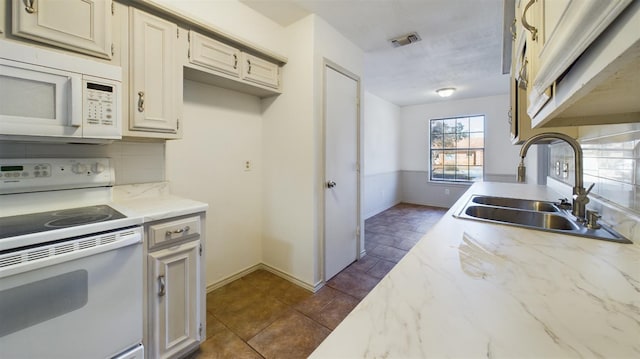 kitchen with sink, white appliances, dark tile patterned floors, tasteful backsplash, and cream cabinetry