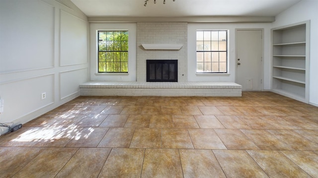 unfurnished living room with a brick fireplace, built in features, and light tile patterned floors