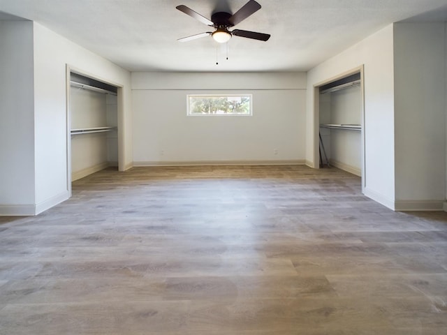 unfurnished bedroom with ceiling fan, two closets, and light wood-type flooring