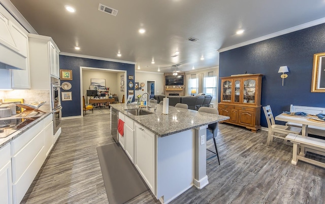 kitchen featuring sink, white cabinetry, a kitchen breakfast bar, an island with sink, and dark stone counters