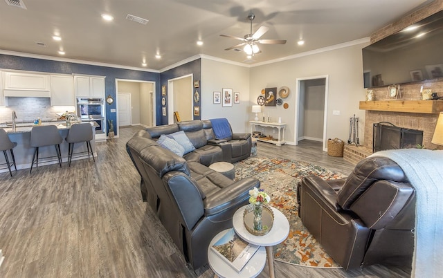 living room featuring sink, dark hardwood / wood-style flooring, ornamental molding, ceiling fan, and a brick fireplace