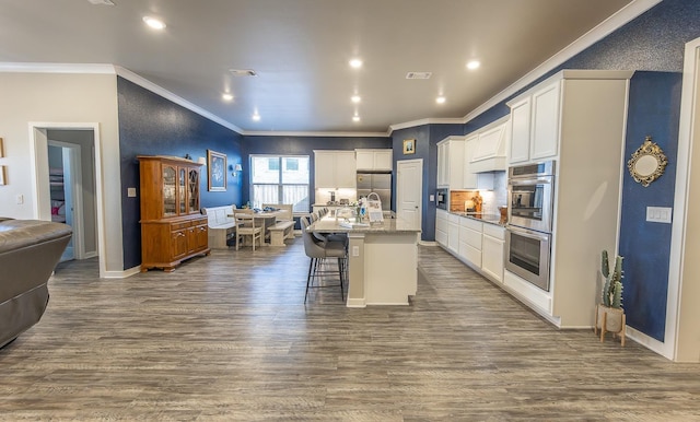 kitchen featuring a breakfast bar area, a center island with sink, ornamental molding, hardwood / wood-style flooring, and light stone countertops