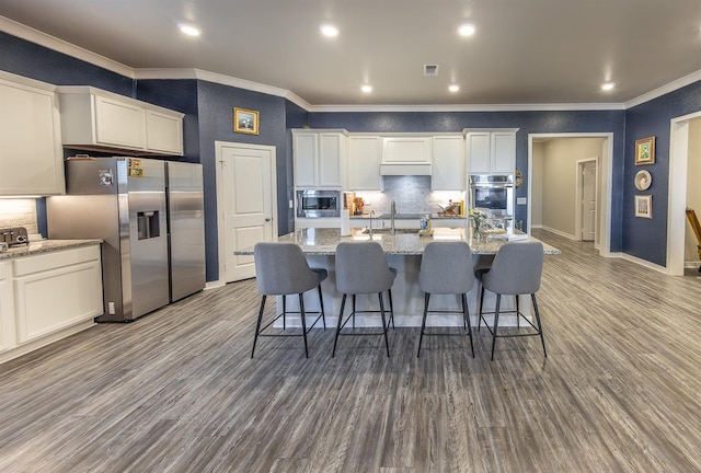 kitchen with sink, a breakfast bar, a kitchen island with sink, stainless steel appliances, and light stone counters