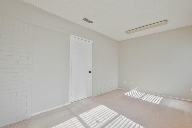 empty room with brick wall, light carpet, and a textured ceiling