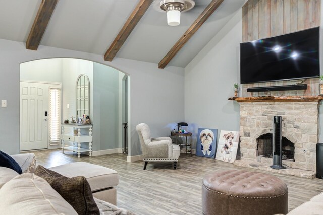 living room featuring high vaulted ceiling, a stone fireplace, hardwood / wood-style floors, and beam ceiling