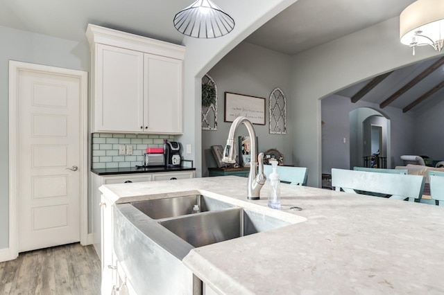 kitchen featuring sink, light hardwood / wood-style flooring, hanging light fixtures, backsplash, and white cabinets