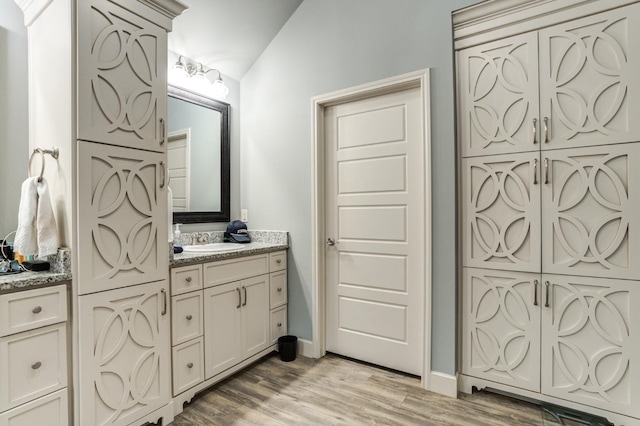 bathroom with vanity, wood-type flooring, and vaulted ceiling