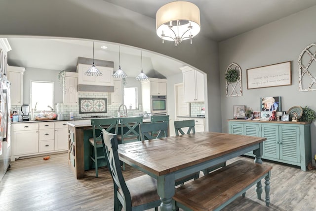 dining area with lofted ceiling, sink, an inviting chandelier, and light wood-type flooring