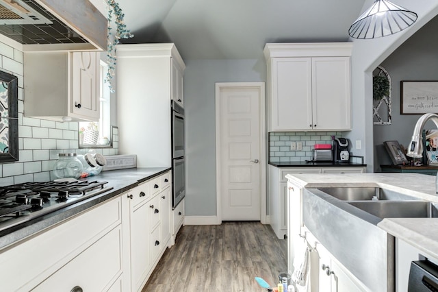 kitchen featuring white cabinetry, tasteful backsplash, appliances with stainless steel finishes, range hood, and light hardwood / wood-style floors