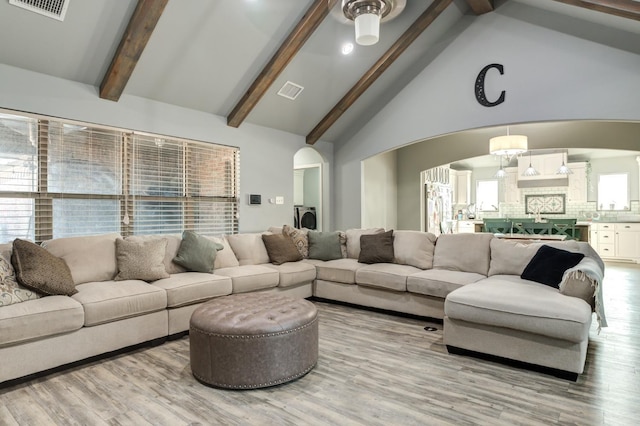 living room with beamed ceiling, washer / dryer, high vaulted ceiling, and light hardwood / wood-style floors