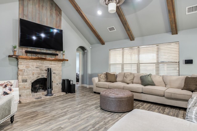 living room featuring wood-type flooring, a stone fireplace, high vaulted ceiling, and beam ceiling