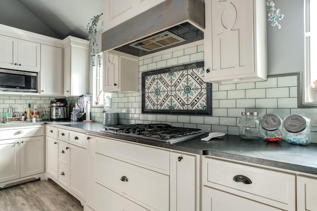 kitchen featuring appliances with stainless steel finishes, lofted ceiling, white cabinets, custom range hood, and light hardwood / wood-style flooring