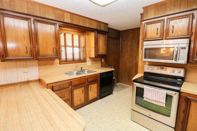 kitchen featuring stainless steel appliances, sink, a textured ceiling, and wood walls