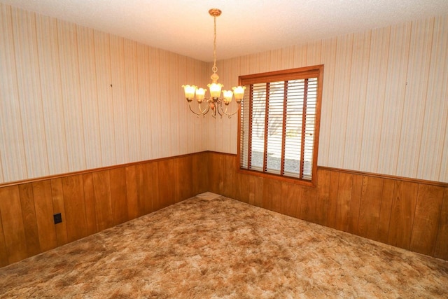 carpeted spare room featuring an inviting chandelier and wood walls