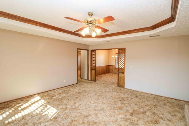 carpeted empty room with a tray ceiling, ornamental molding, a textured ceiling, ceiling fan with notable chandelier, and wood walls