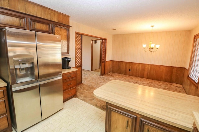 kitchen with hanging light fixtures, an inviting chandelier, stainless steel fridge, and a textured ceiling