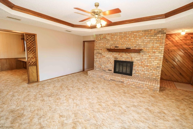 unfurnished living room featuring a brick fireplace, a textured ceiling, carpet flooring, wooden walls, and a tray ceiling