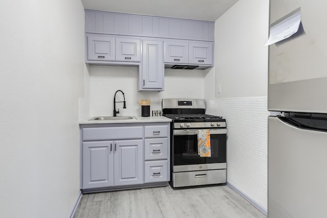 kitchen with sink, stainless steel gas stove, refrigerator, tile walls, and light hardwood / wood-style floors