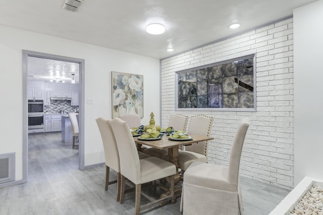 dining space featuring brick wall and light wood-type flooring