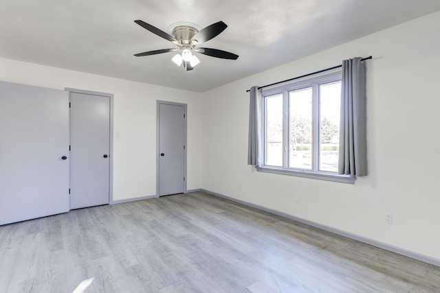 unfurnished bedroom featuring ceiling fan, multiple closets, and light wood-type flooring