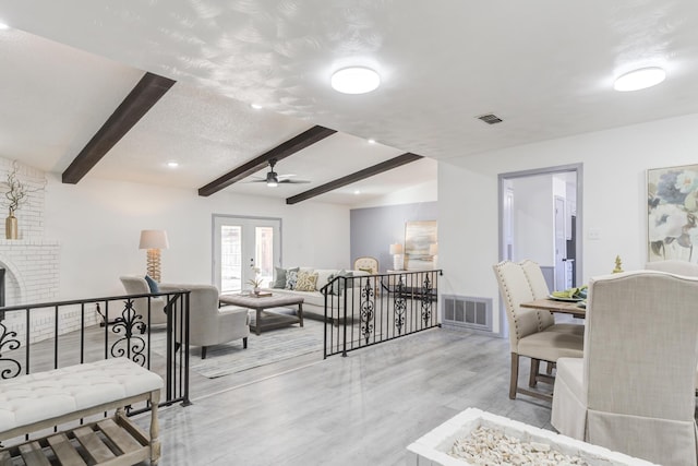 living room with light hardwood / wood-style flooring, lofted ceiling with beams, a textured ceiling, a brick fireplace, and french doors