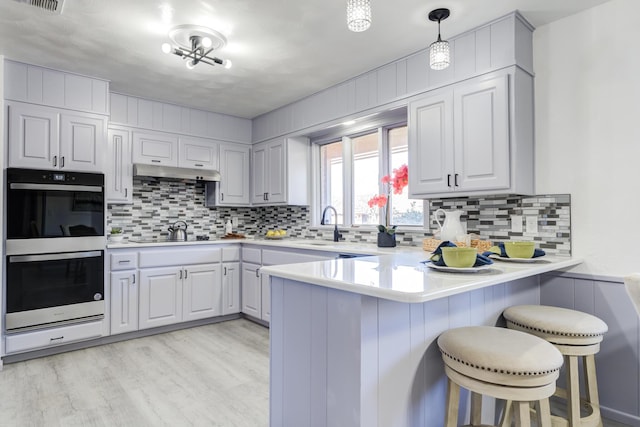 kitchen with a breakfast bar area, hanging light fixtures, light hardwood / wood-style flooring, kitchen peninsula, and double oven