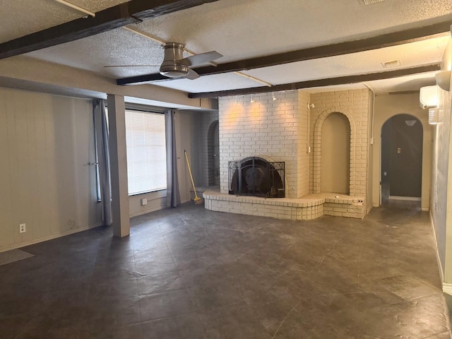 unfurnished living room with ceiling fan, a brick fireplace, a textured ceiling, and beam ceiling