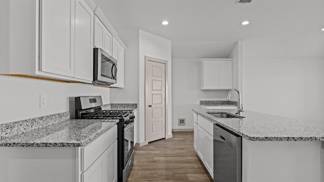 kitchen with sink, stainless steel appliances, light stone counters, white cabinets, and a center island with sink