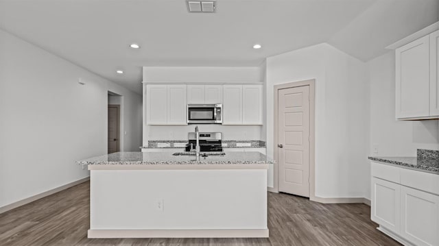 kitchen featuring light stone countertops, white cabinetry, appliances with stainless steel finishes, and a kitchen island with sink