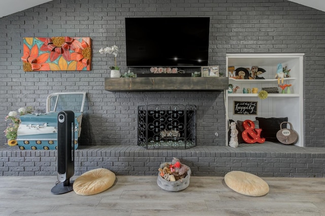 living room featuring built in shelves, wood-type flooring, vaulted ceiling, and a brick fireplace