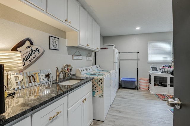 kitchen with sink, washer and dryer, white cabinets, dark stone counters, and light wood-type flooring