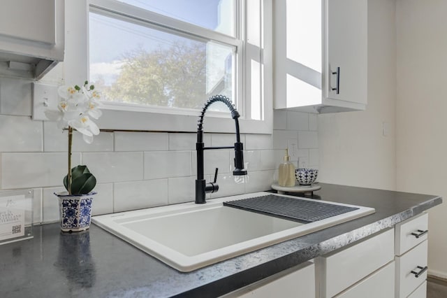 interior details featuring dark countertops, tasteful backsplash, white cabinets, and a sink