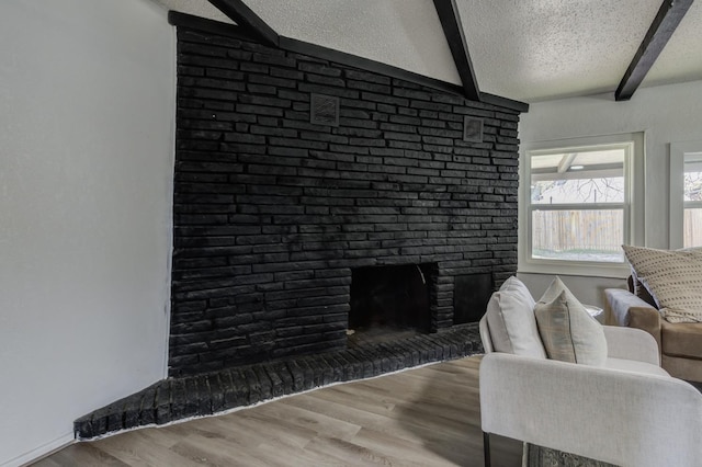 living room with a textured ceiling, beam ceiling, a fireplace, and wood finished floors