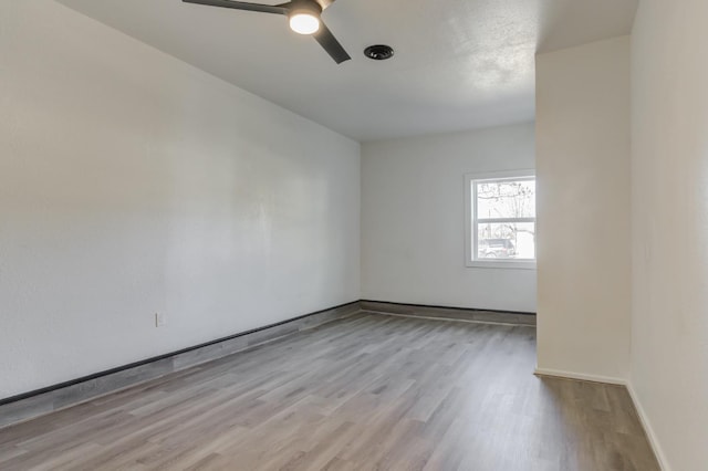 spare room featuring ceiling fan, light wood-type flooring, and baseboards