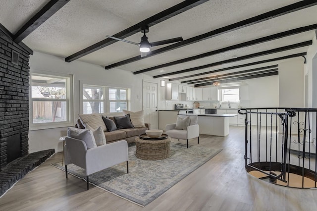 living room with light wood-style floors, beam ceiling, a fireplace, and a textured ceiling