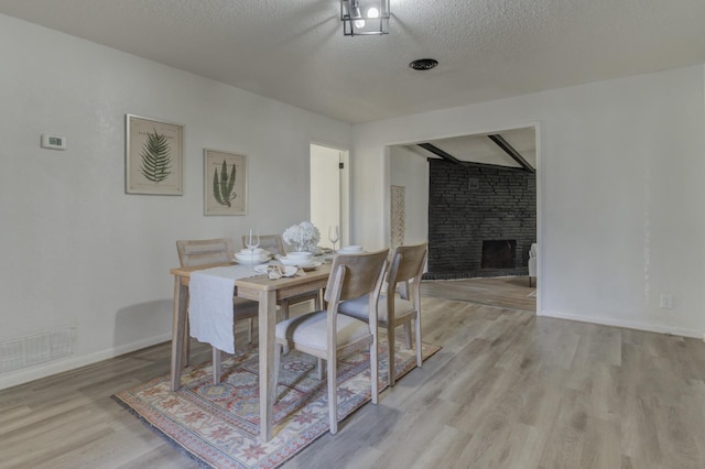 dining area with a fireplace, visible vents, light wood-style flooring, a textured ceiling, and baseboards