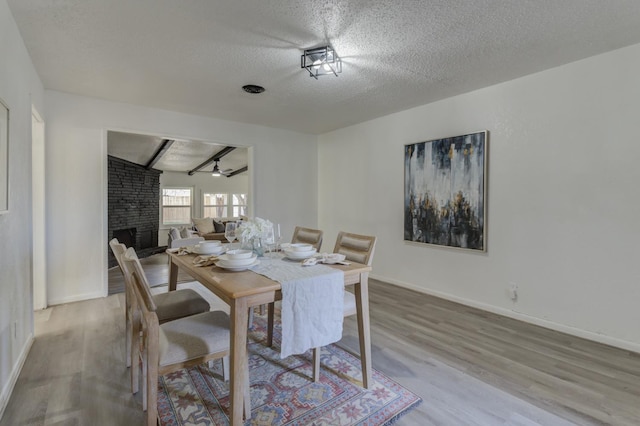 dining space featuring baseboards, wood finished floors, beamed ceiling, a textured ceiling, and a fireplace