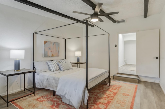 bedroom with light wood finished floors, visible vents, ceiling fan, vaulted ceiling with beams, and a textured ceiling