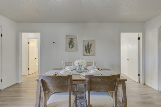 dining room with a textured ceiling, light wood finished floors, and baseboards