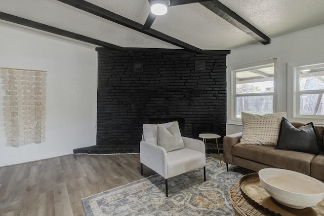 living room featuring a large fireplace, beamed ceiling, a textured ceiling, and wood finished floors