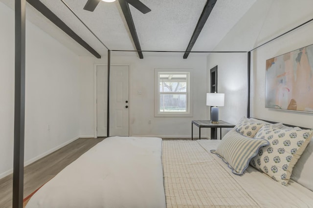 bedroom featuring a textured ceiling, baseboards, beam ceiling, and wood finished floors