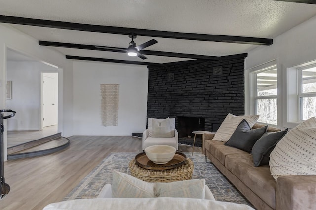 living area featuring a textured ceiling, a fireplace, wood finished floors, a ceiling fan, and beam ceiling