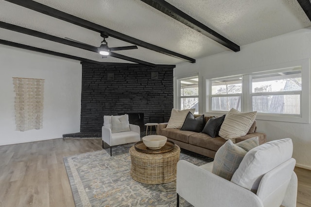 living area with a textured ceiling, a fireplace, wood finished floors, a ceiling fan, and beam ceiling